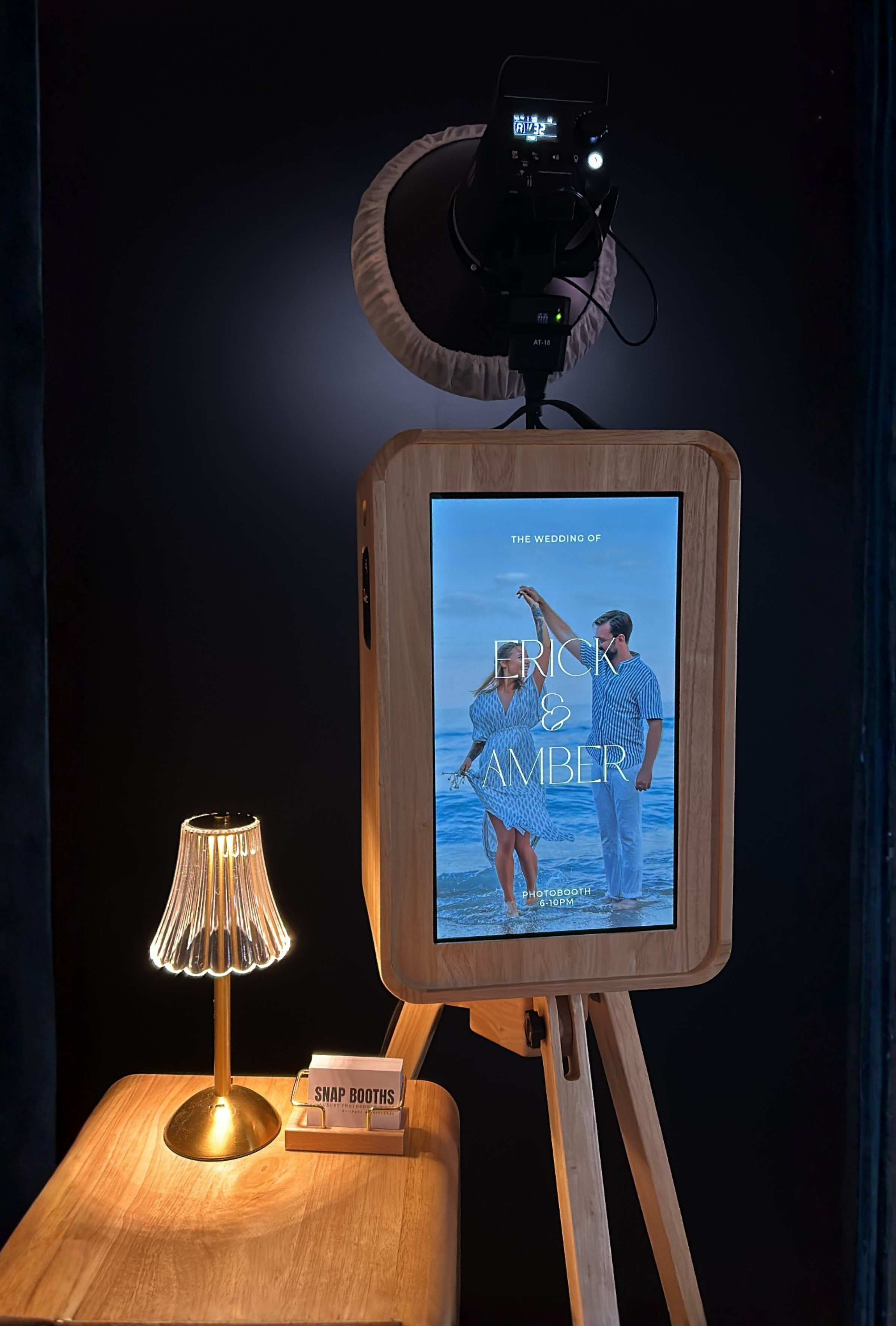 Photobooth setup with camera, screen, and lamp on a dark background