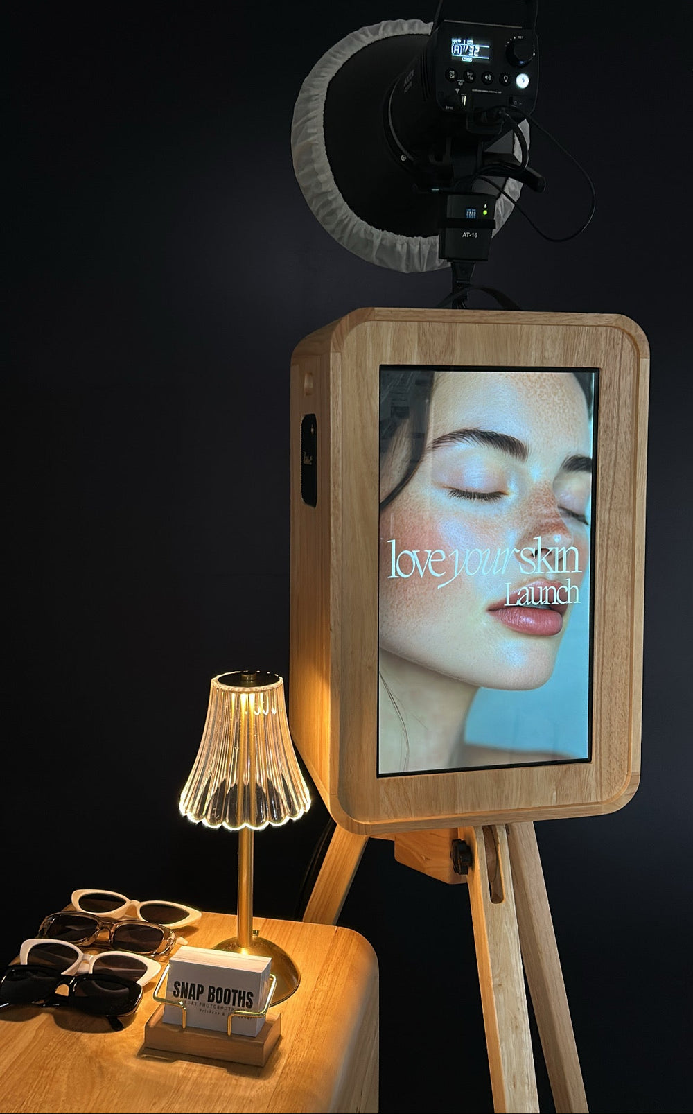 Smartphone with screen displaying a product on a stand with a lamp and sunglasses in the background.