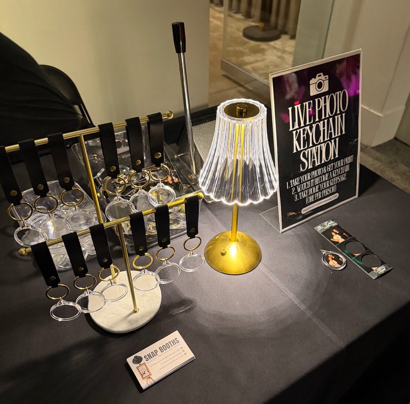 Decorative lamp with a stand on a table, next to a sign for a live photo keychain station.